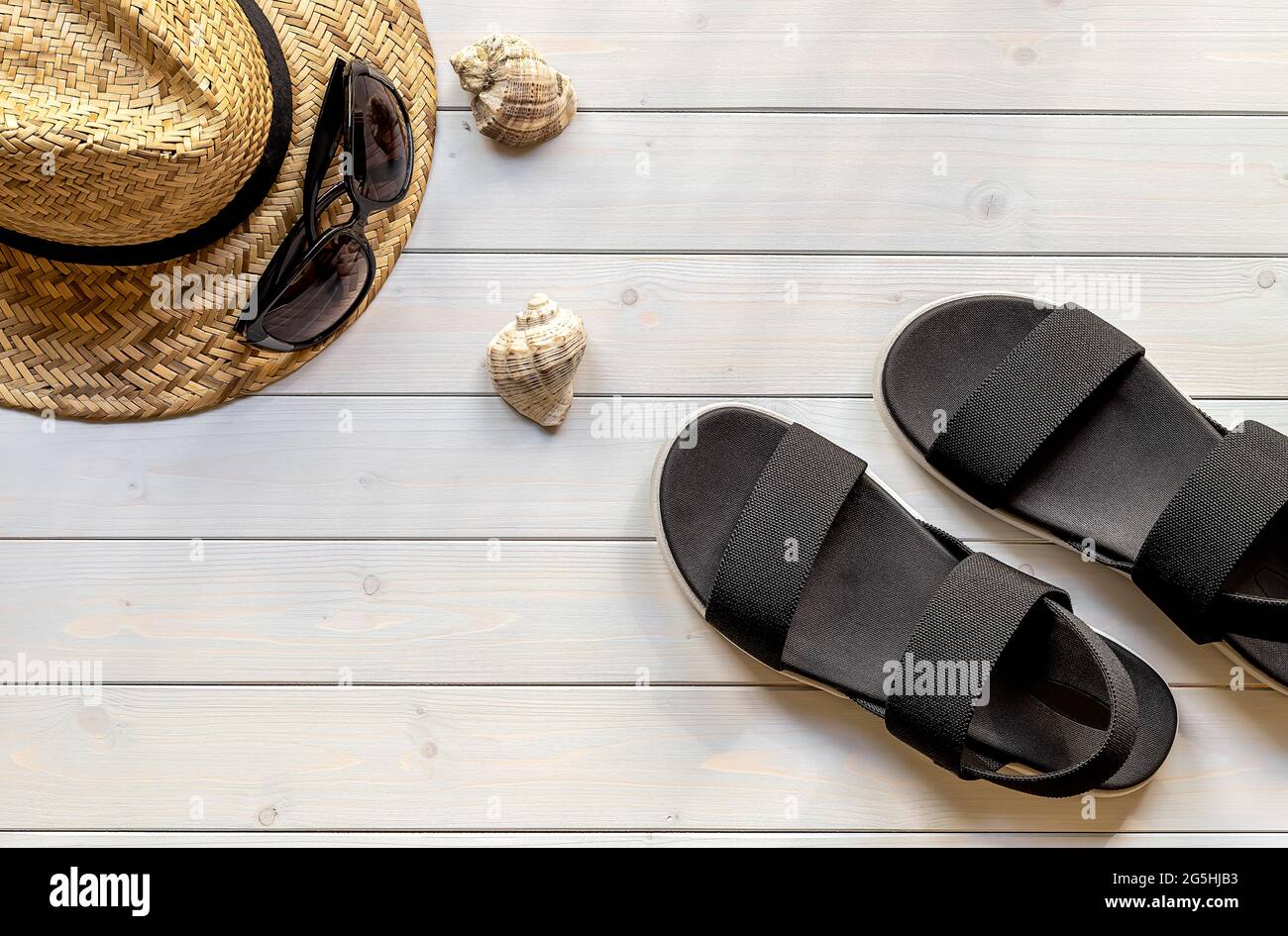 Women's open-toe black sandals from recycled plastic fibers, straw hat, sunglasses, and seashells  Stock Photo
