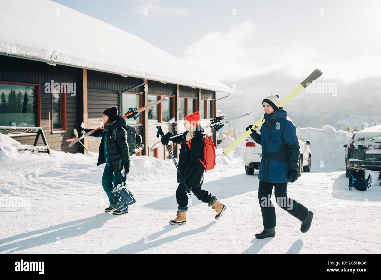 Full length of friends walking with skis at tourist resort during sunny day Stock Photo