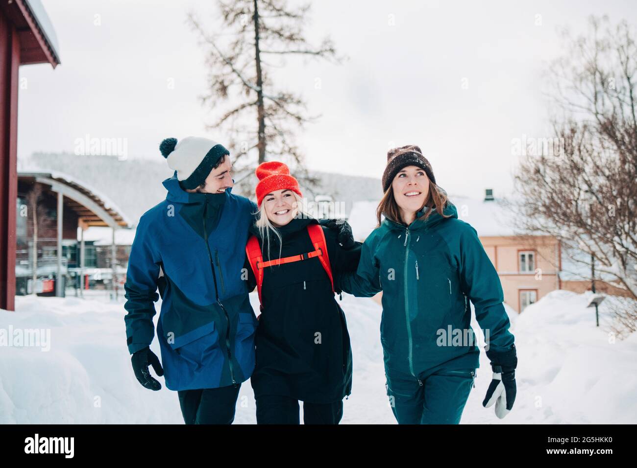 Cheerful male and female friends walking with arm around at ski resort Stock Photo