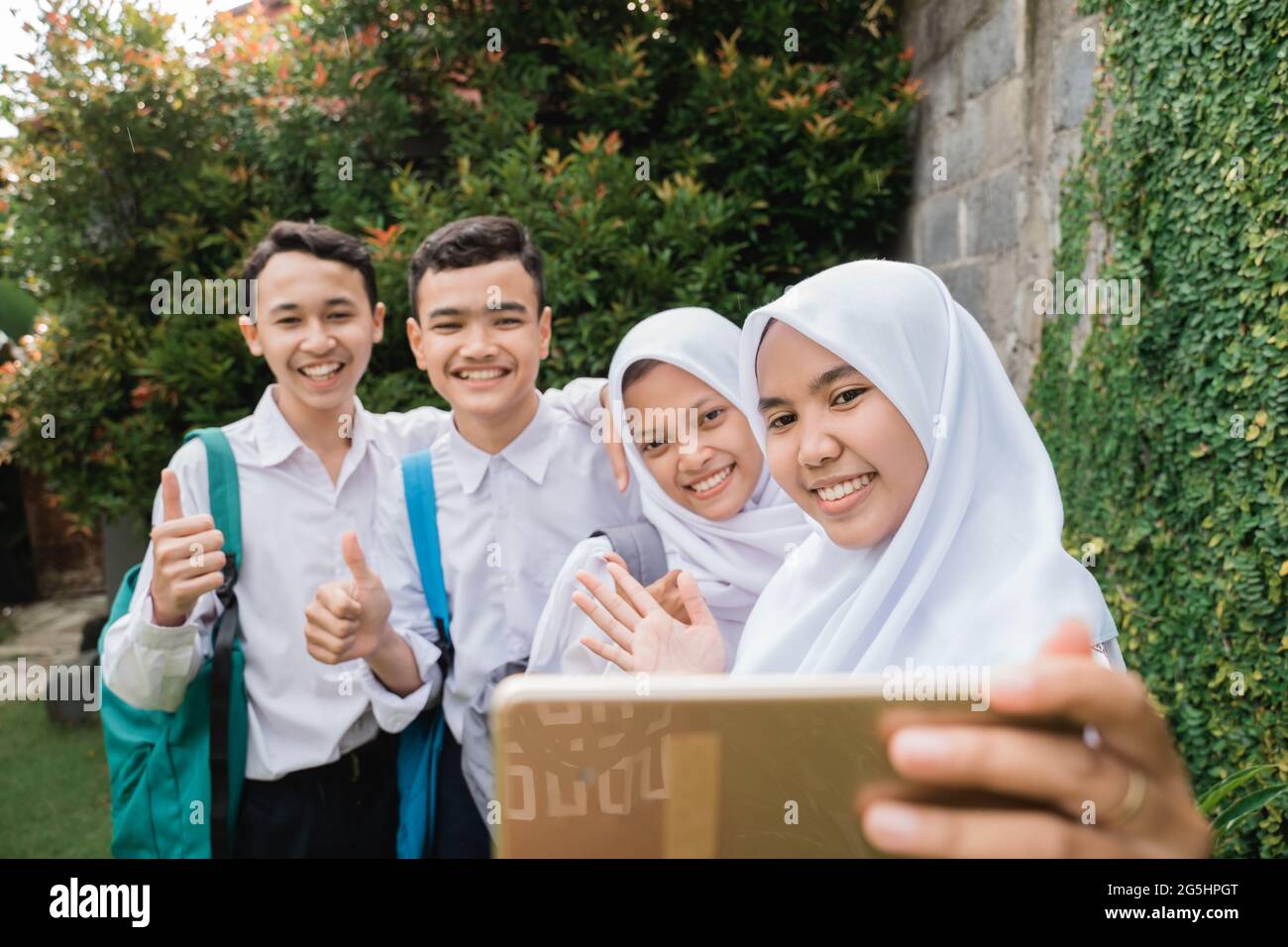 four teenagers in junior high school uniforms taking selfie together using a smartphone Stock Photo