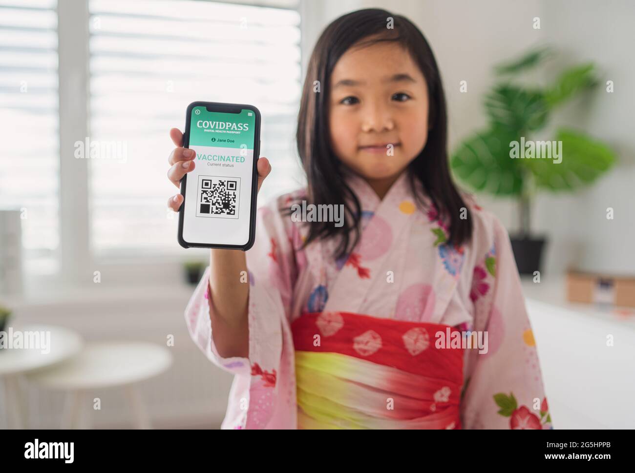 Small japanese child with traditional costume showing covid-19 vaccination certificate on smartphone. Stock Photo