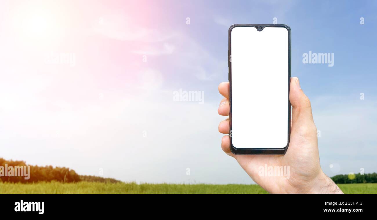 Empty screen smartphone background. Hand with blank smartphone on background of summer sunny calm landscape with country village meadow, forest and sky. High quality photo Stock Photo