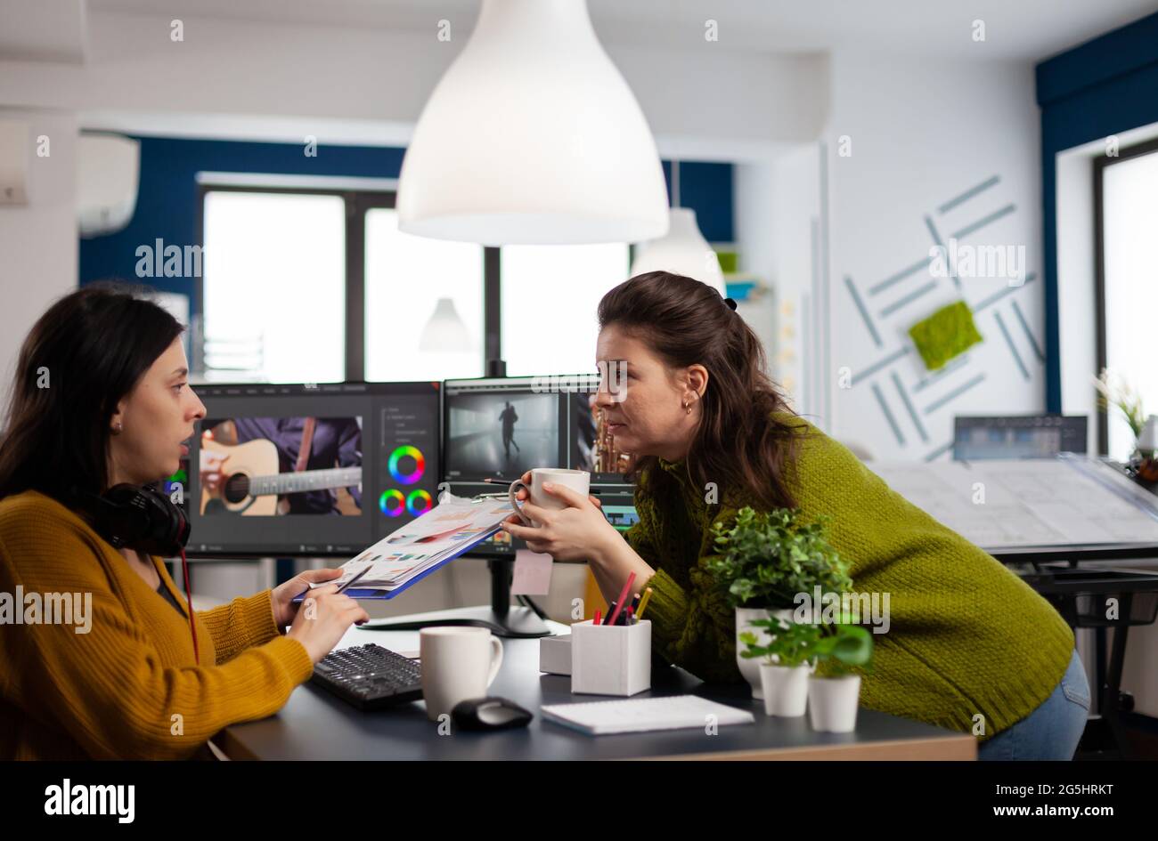 Art video director explaning to woman videographer the steps for prosessing film montage showing clipboard with informations. Video editor working in post production software in creative agency Stock Photo