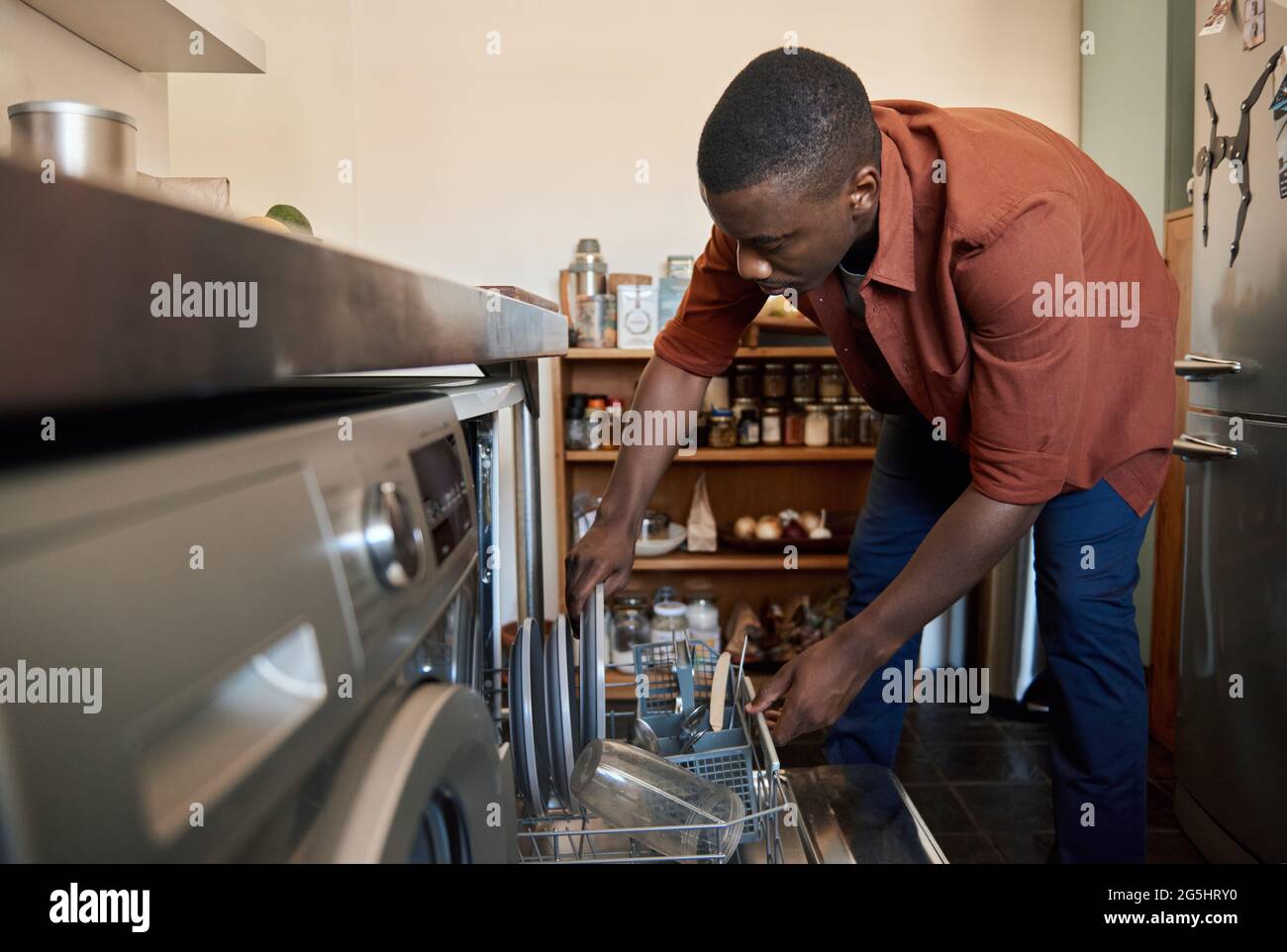 Young African man putting plates in his dishwasher at home Stock Photo