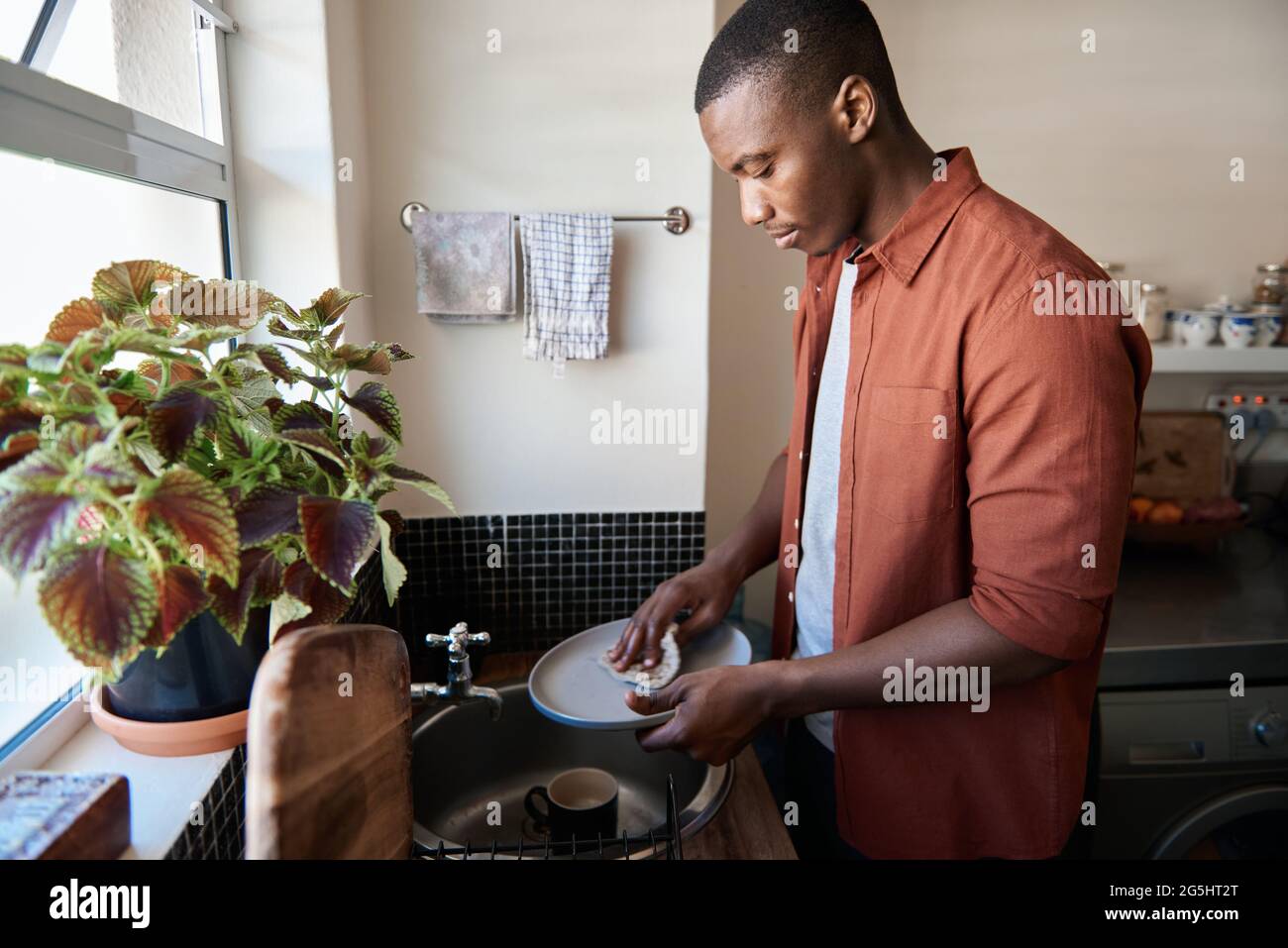 Young African man washing dishes in his kitchen sink at home Stock Photo