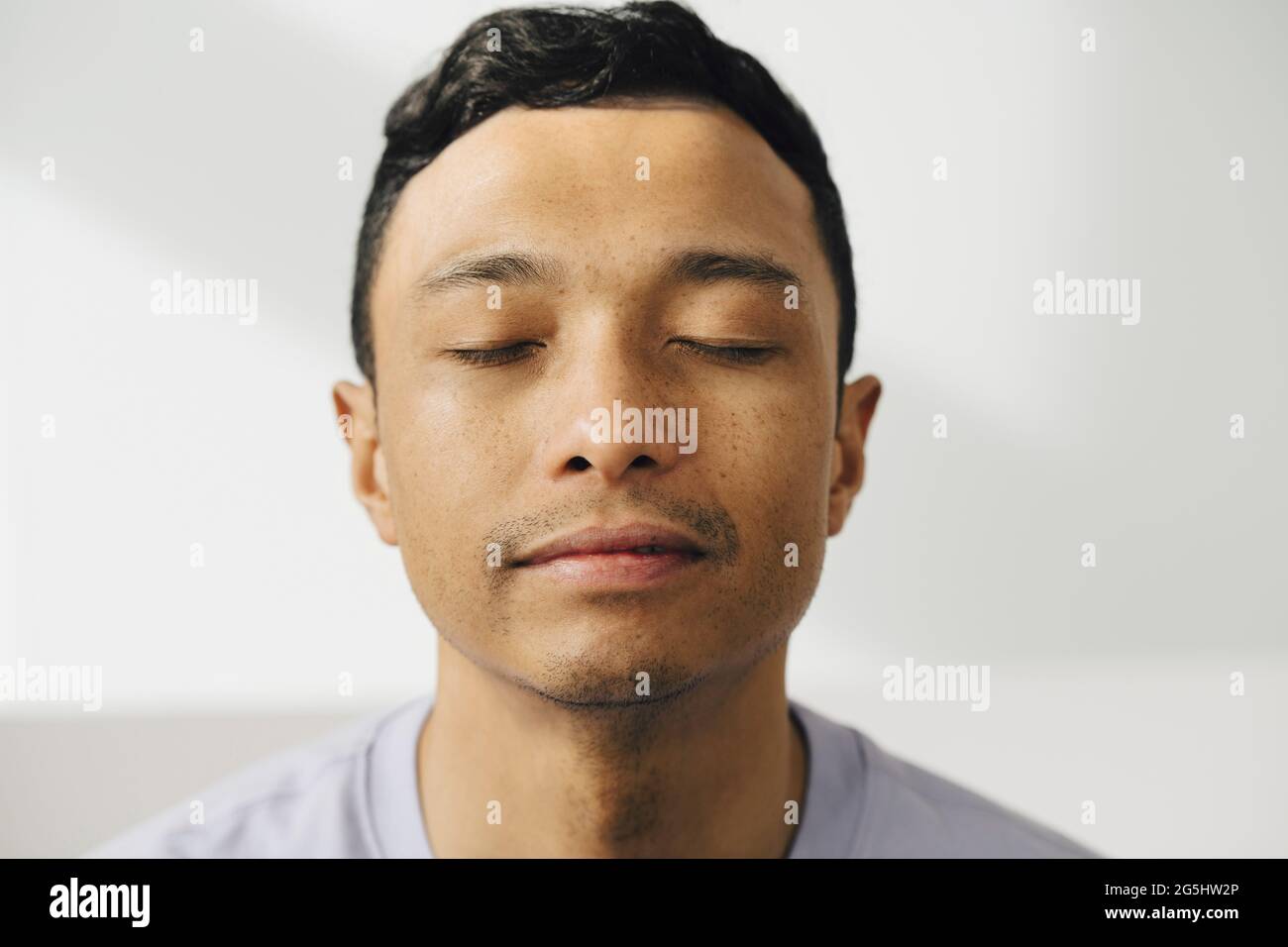 Man with black hair against white wall Stock Photo