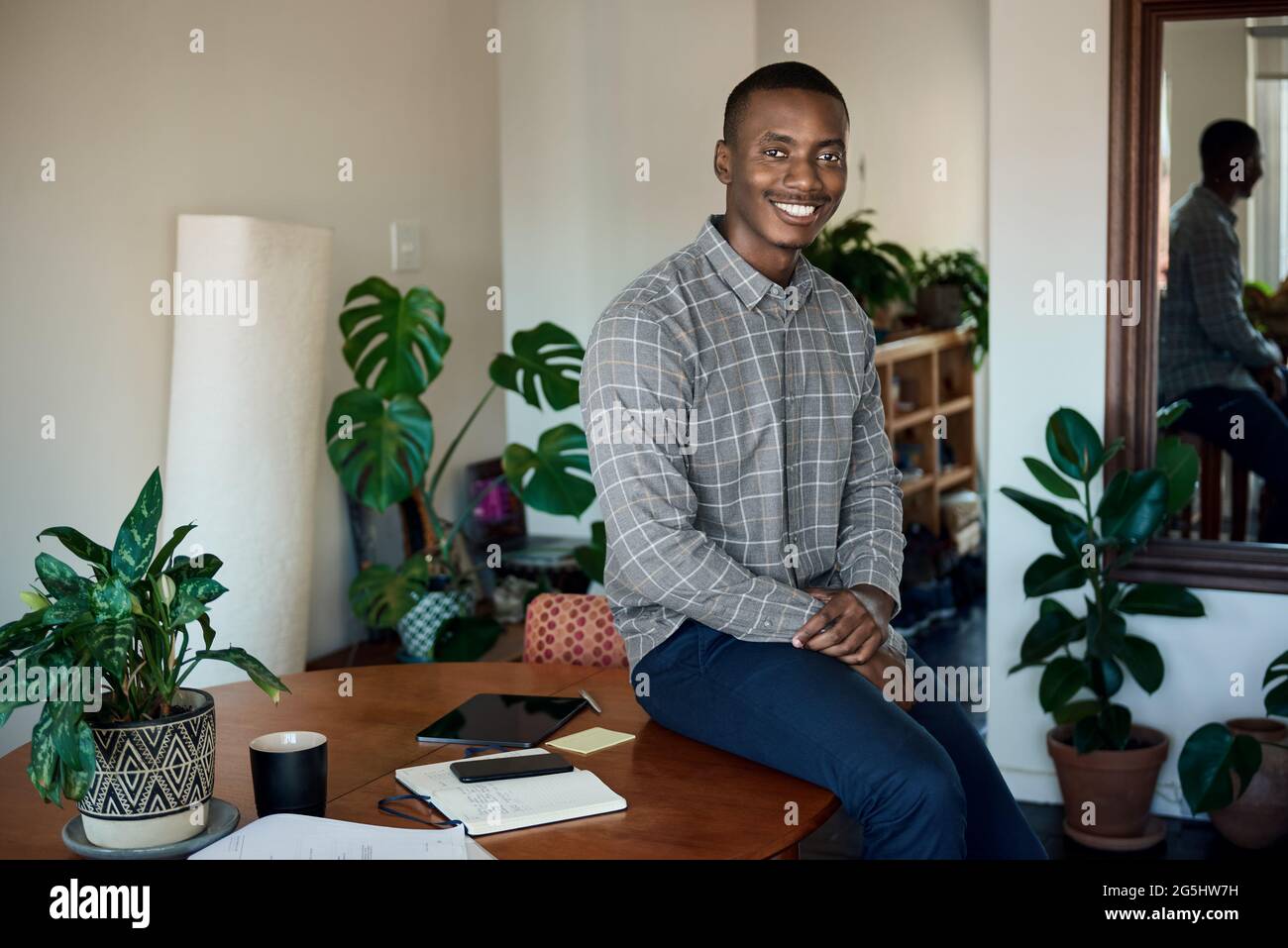 Smiling African businessman sitting on a table while working from home Stock Photo