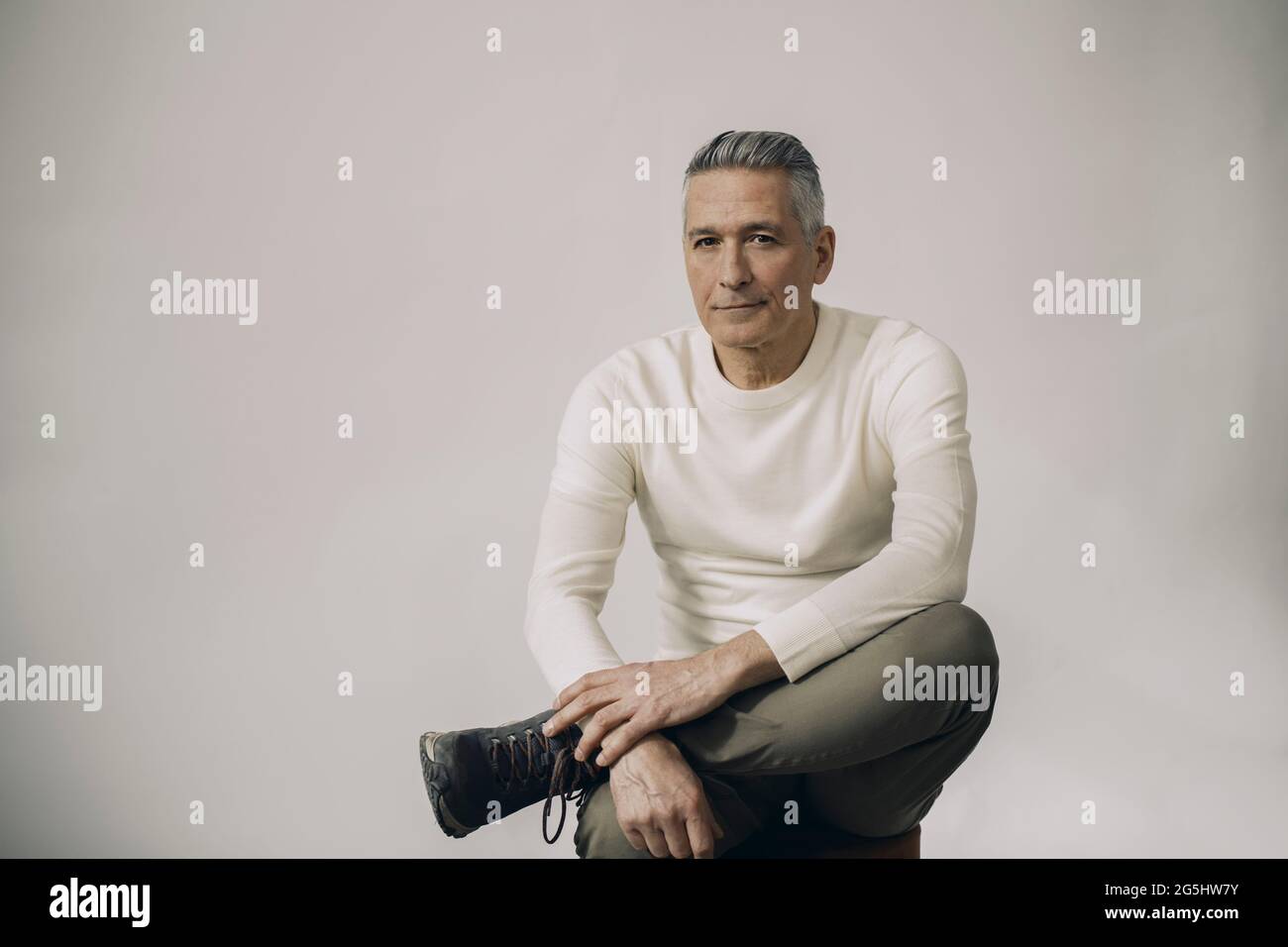 Full length portrait of mature man sitting against white background Stock Photo