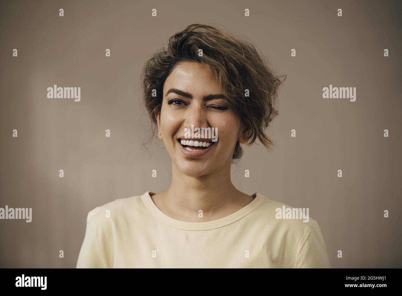 Happy woman winking eye against beige background Stock Photo