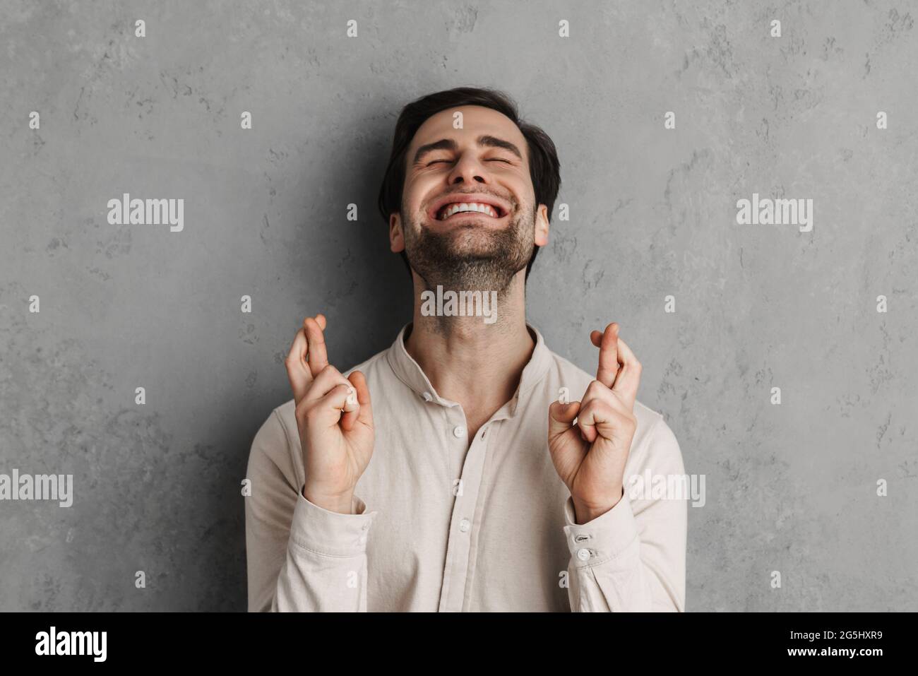 Young happy handsome man wearing casual clothes standing over isolated gray background gesturing finger crossed. Luck and superstitious concept. Stock Photo
