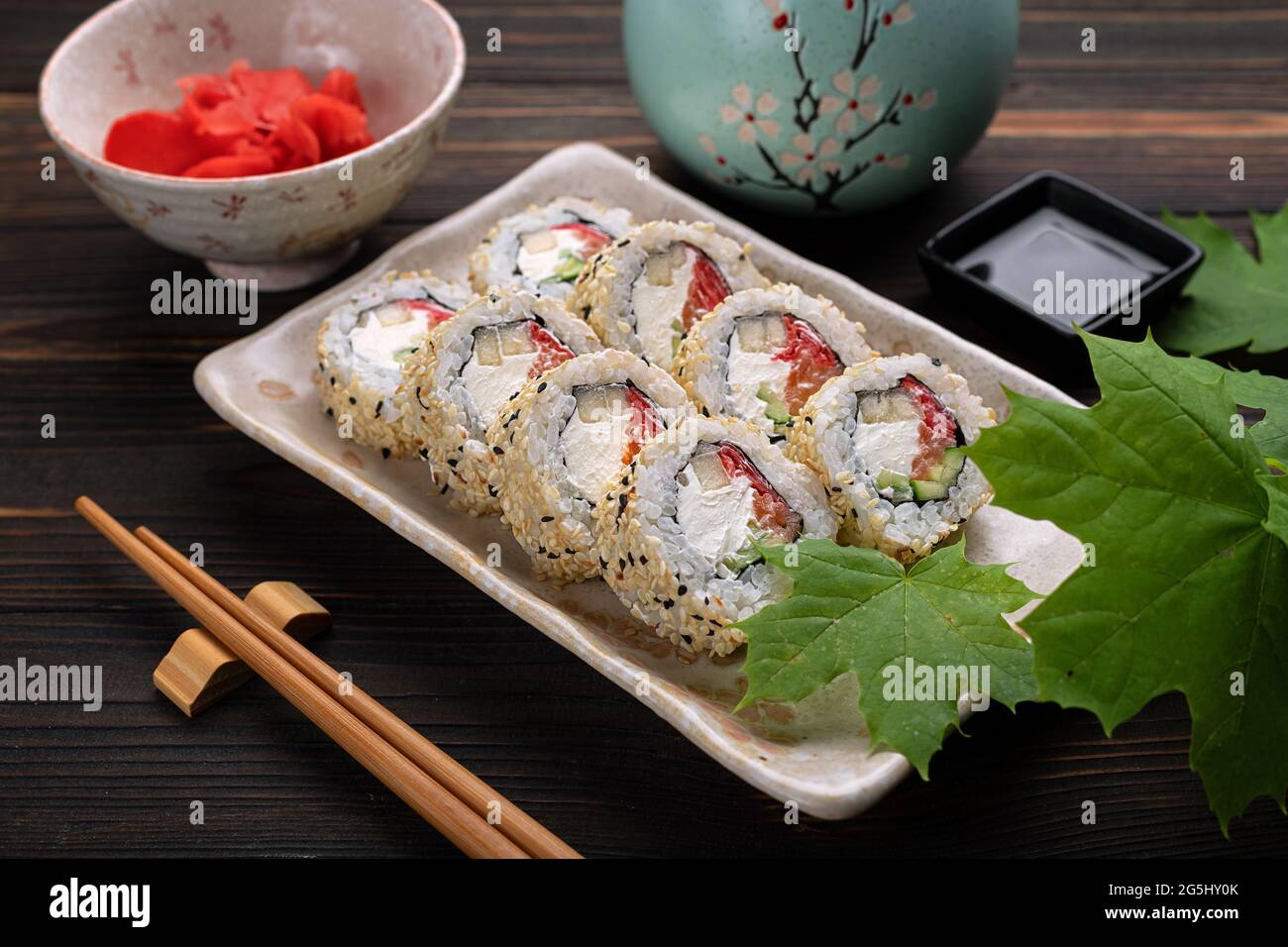 Set of sushi rolls with cream cheese, rice and salmon on a board decorated with ginger on a dark wooden background. Japanese cuisine. Food photo Stock Photo