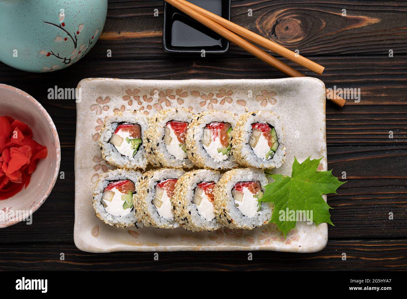 Set of sushi rolls with cream cheese, rice and salmon on a board decorated with ginger on a dark wooden background. Japanese cuisine. Food photo Stock Photo
