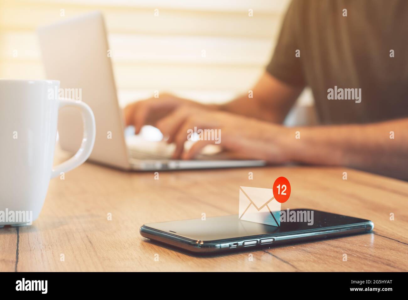 E-mail message notification pops up on mobile smart phone in home office, man typing laptop computer, selective focus Stock Photo