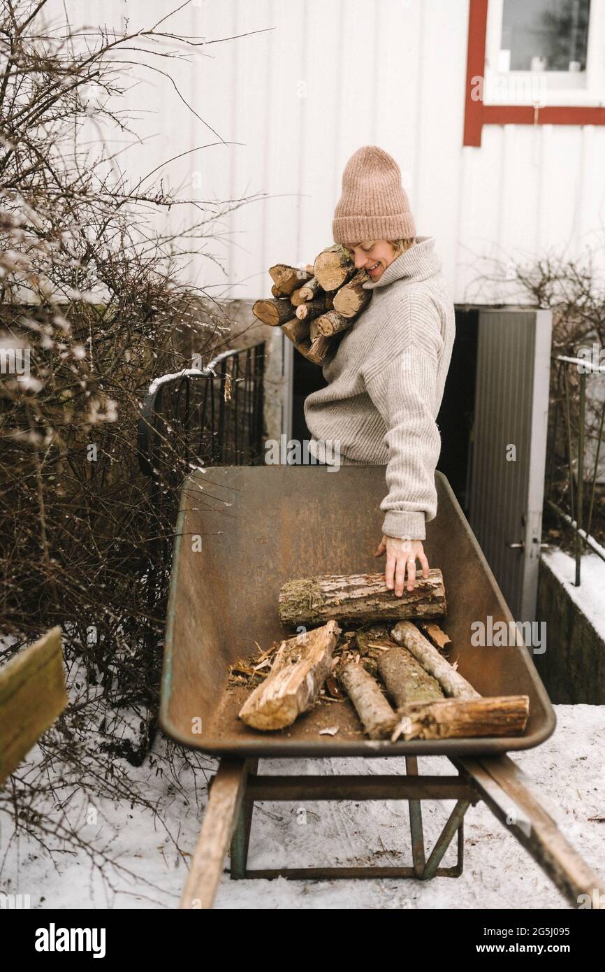 Woman collecting firewood from wheelbarrow during winter Stock Photo