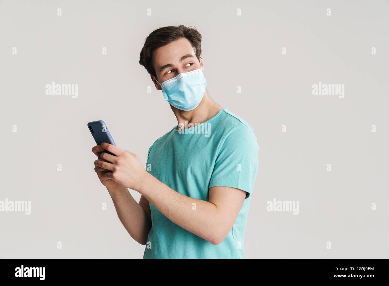 Joyful handsome guy in protective mask using mobile phone isolated over white wall Stock Photo
