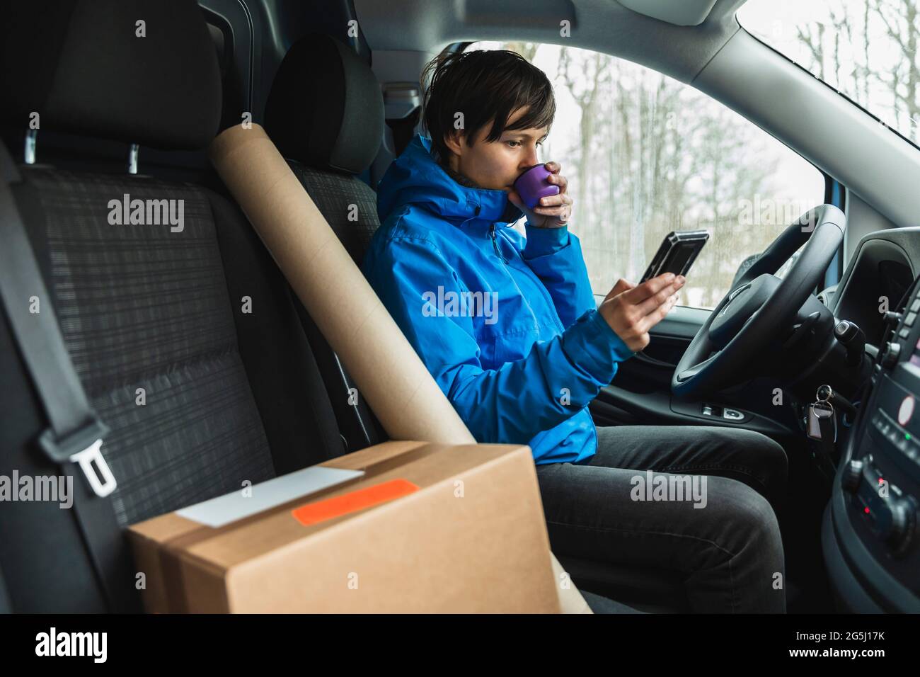 Female essential service driver drinking coffee while using smart phone