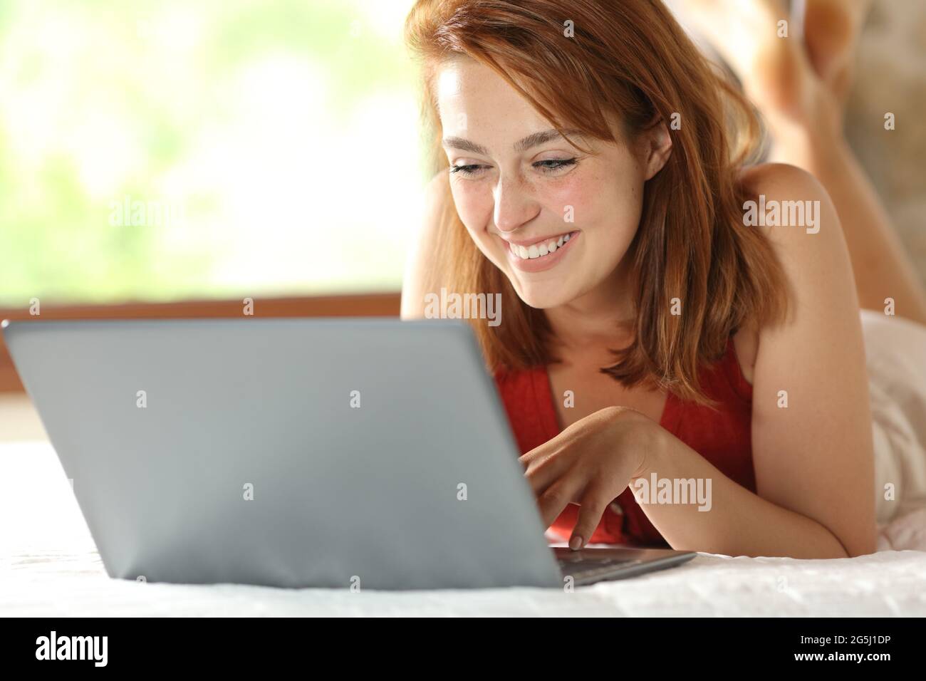 Happy woman checking laptop lying on the bed in the bedroom at home Stock Photo