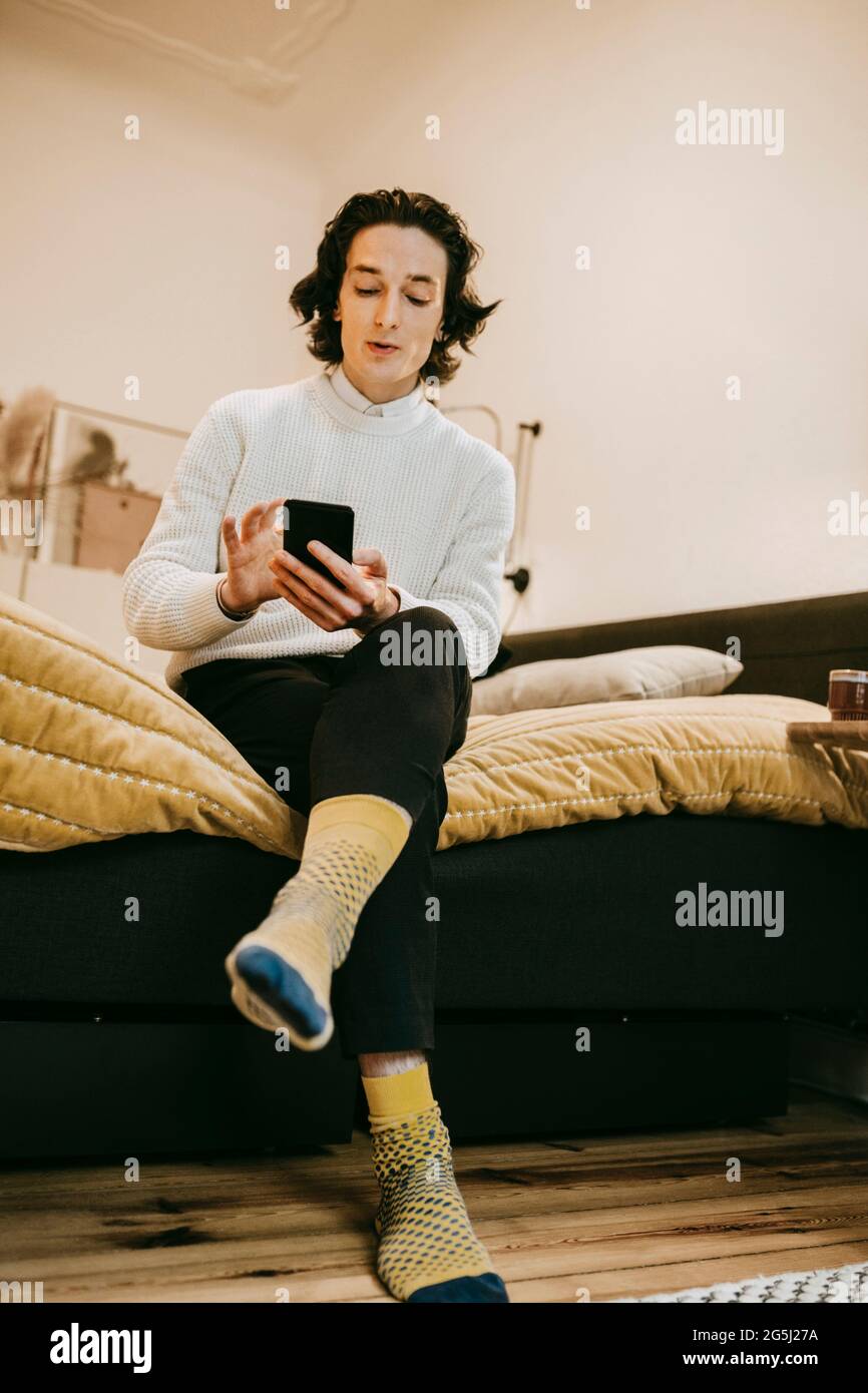 Man using smart phone while sitting bedroom at home Stock Photo