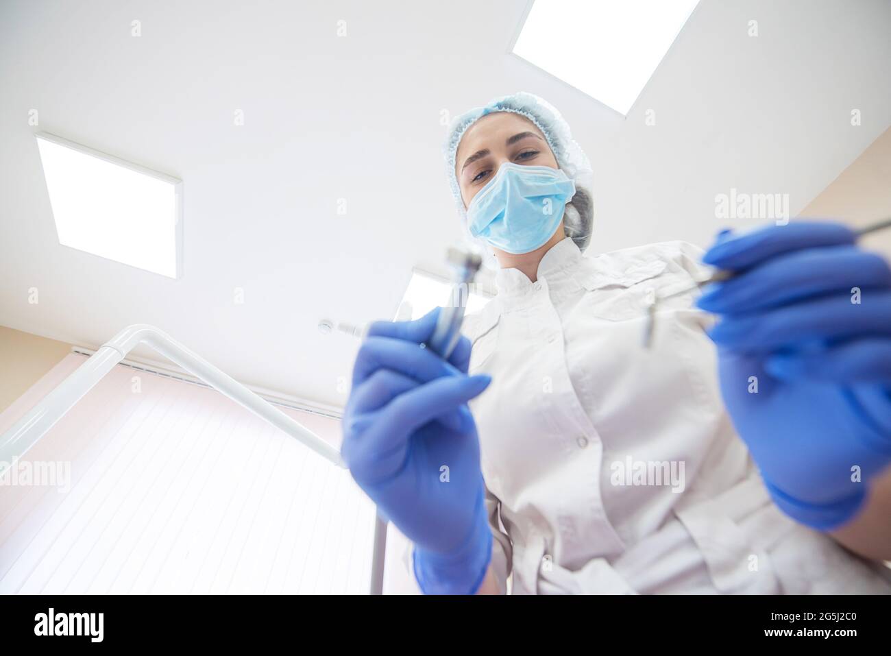 Attractive smiling woman doctor in a white uniform with tools in hand. Young beautiful female dentist in mask and gloves with the eyes of a patient Stock Photo