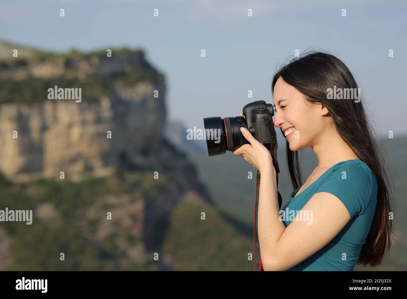 Side view portrait of a happy asian woman taking photos with a dslr camera outdoors in the mountain Stock Photo