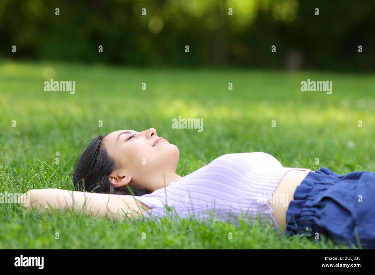 Mixed race woman relaxing lying on the grass in a green park Stock Photo