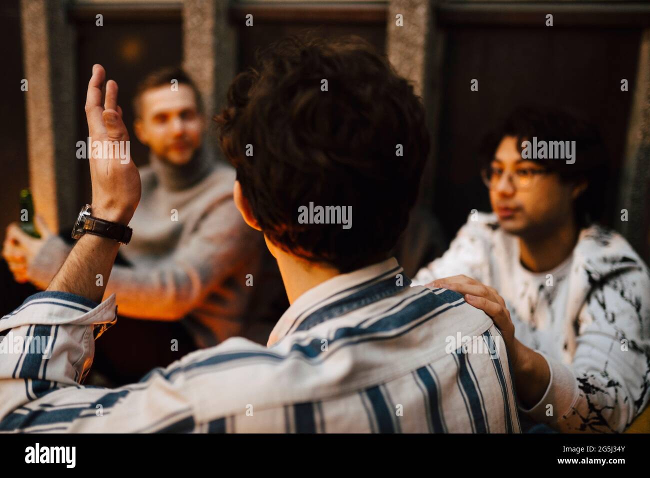 Rear view of man gesturing while talking with friends at balcony Stock ...