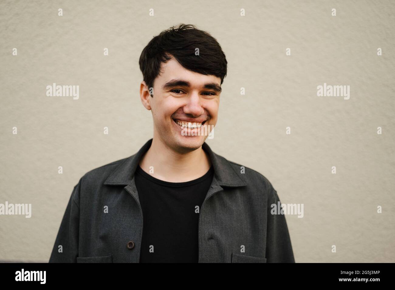 Happy young man with black hair against beige wall Stock Photo