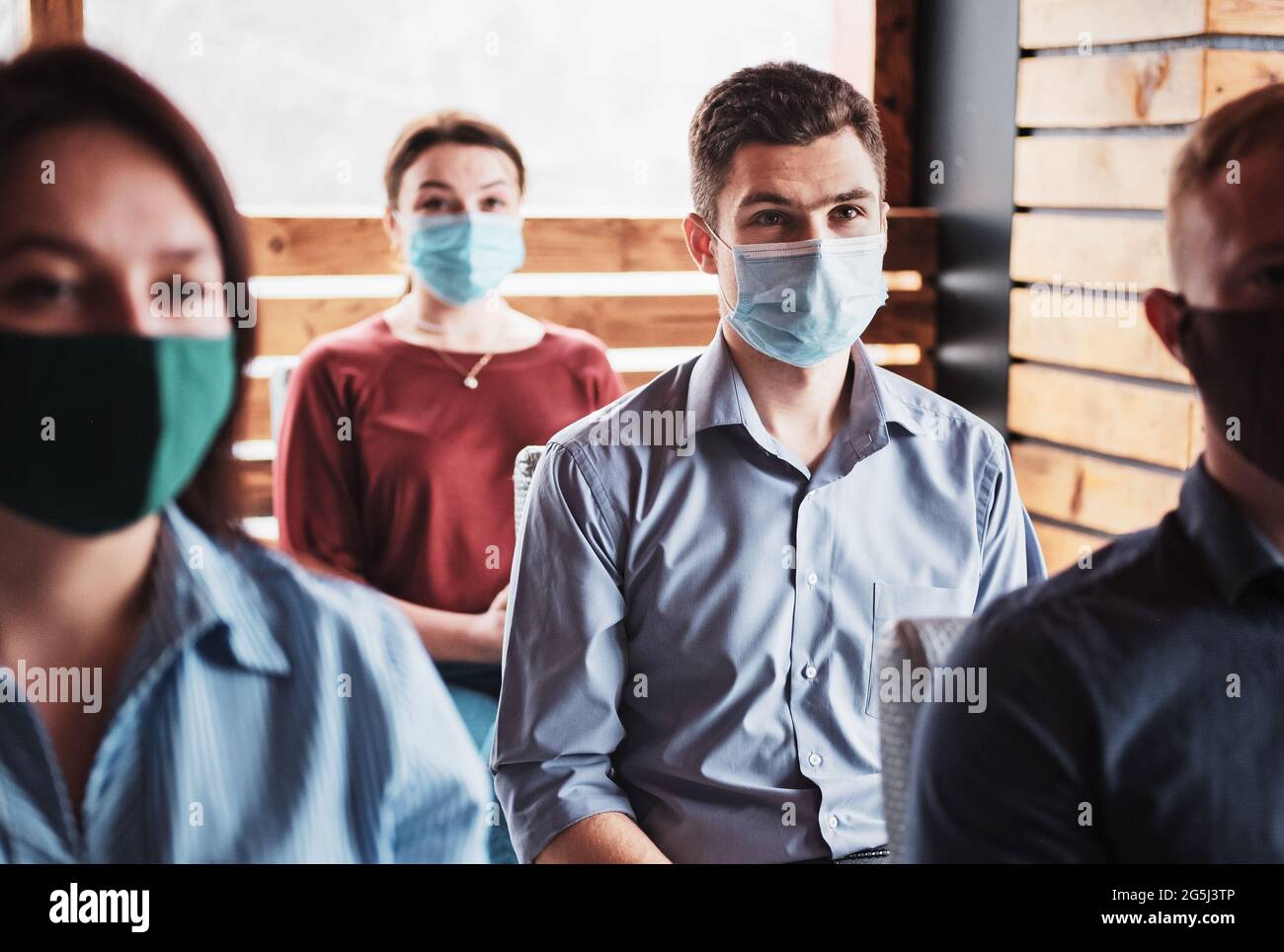 Young people in the new normal wearing masks on their faces are listening to the coach - Millennials are learning from the coronavirus epidemic - Meet Stock Photo