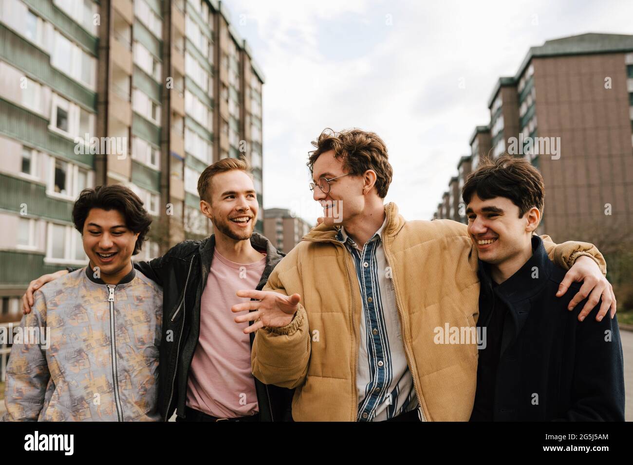 Smiling male friends talking while walking with arms around in city Stock Photo