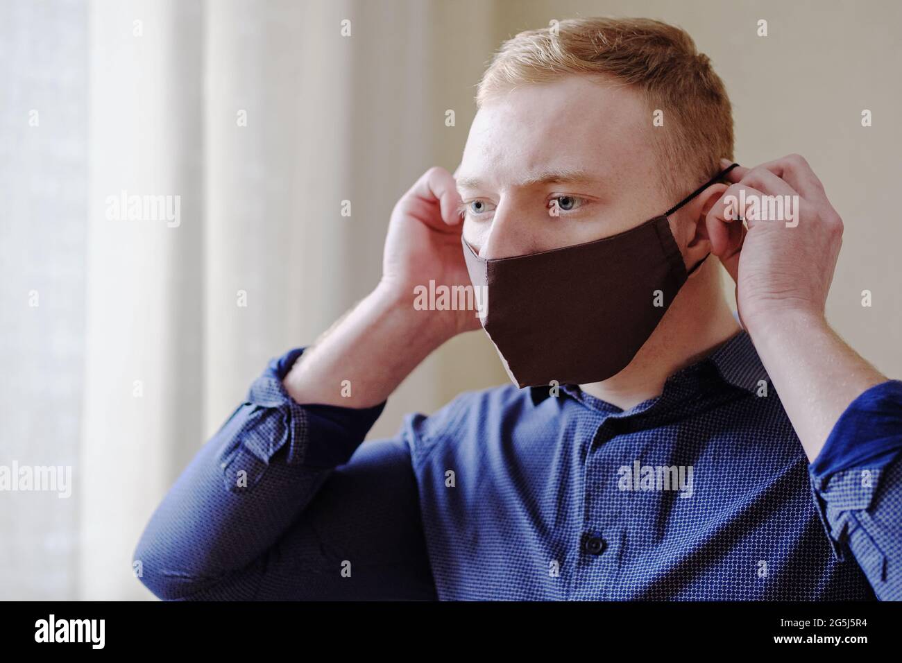 A young man puts on a protective mask on his face as protection against coronavirus - A mask on a man's face during the COVID-19 epidemic - Concept of Stock Photo