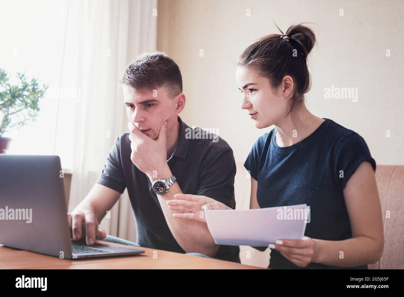 Young couple manages finances budgeting and keeping track of expenses - Husband and wife look through their bank accounts and make payments online usi Stock Photo