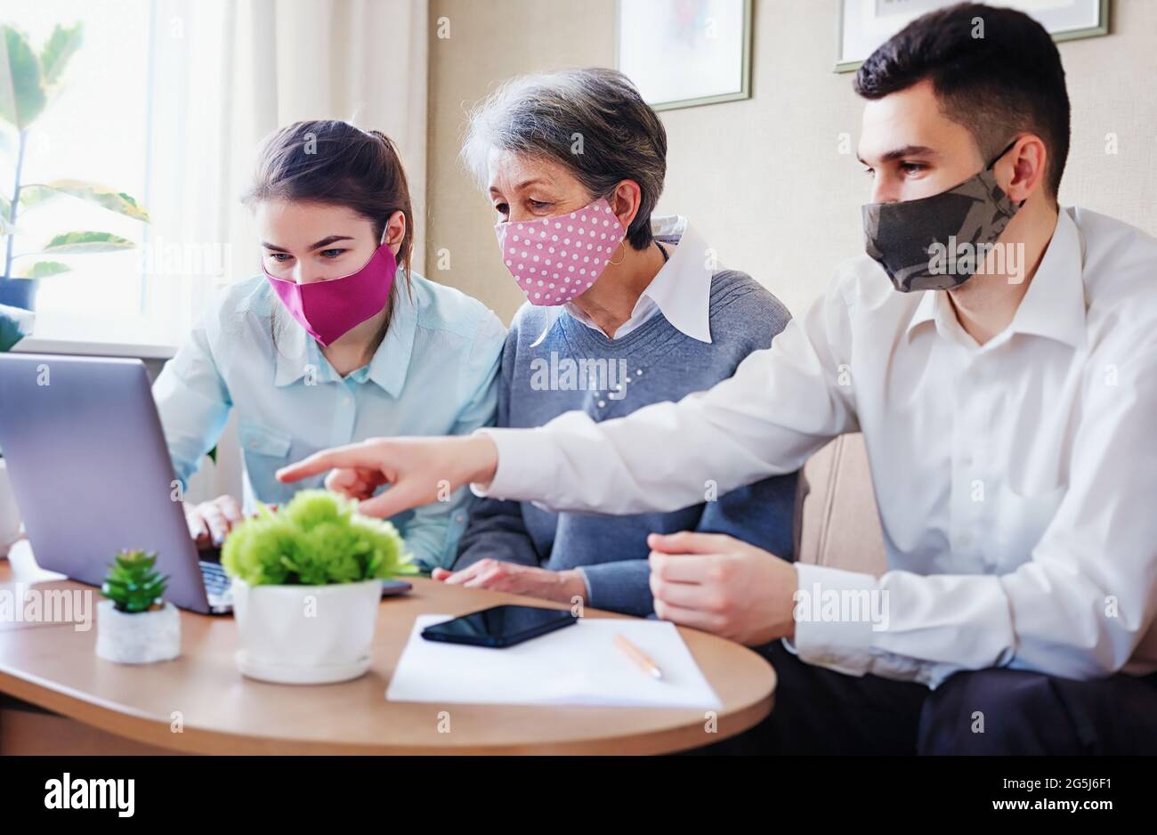 Relatives visit an elderly woman and help her find the necessary information on the Internet - Adult children and a mother wearing masks on her face i Stock Photo