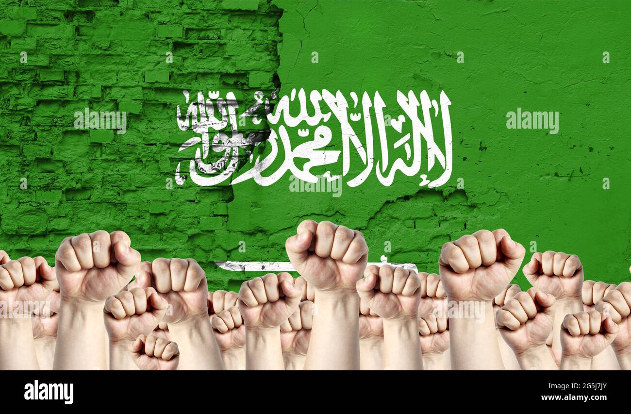 Raised fists of men against the background of the flag of Saudi Arabia painted on the wall, the concept of popular unity and the opinion of the majori Stock Photo