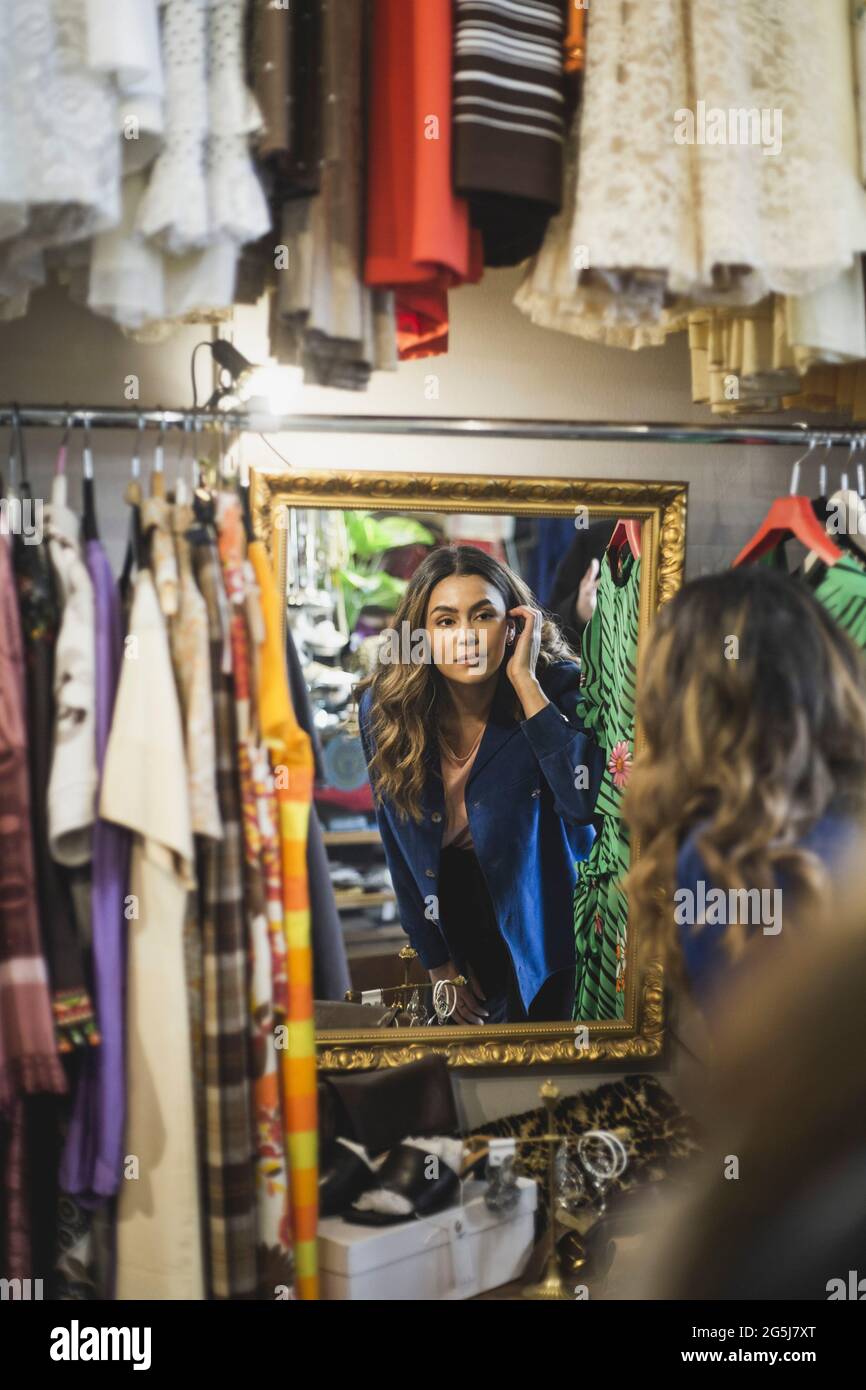 Female owner looking in mirror while standing at clothing store Stock Photo