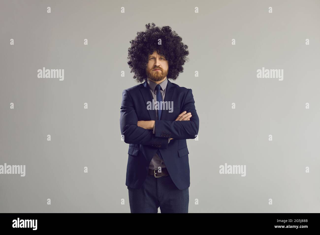 Serious business man in stylish curly hair wig standing with arms crossed Stock Photo