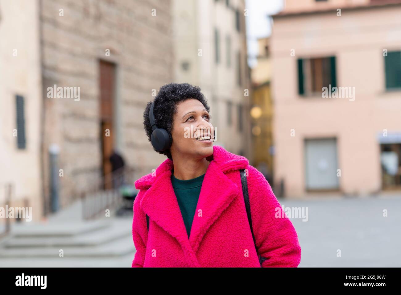 Italy, Tuscany, Pistoia, Woman in pink coat and headphones walking through city Stock Photo
