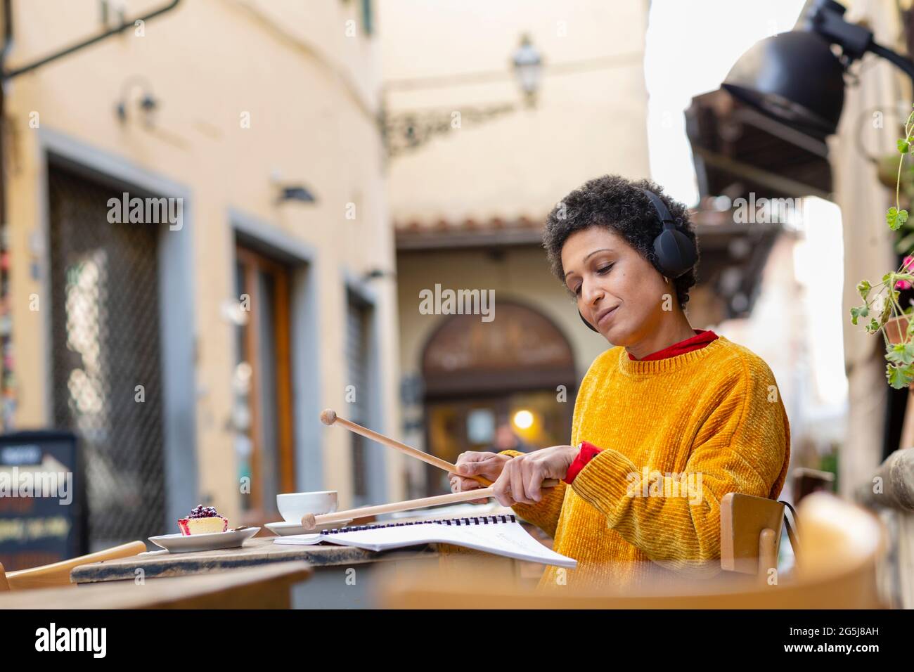 Italy, Tuscany, Pistoia, Woman practicing with drumsticks in outdoor cafe Stock Photo