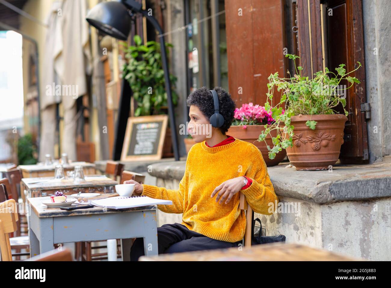 Italy, Tuscany, Pistoia, Woman with headphones sitting in outdoor cafe Stock Photo