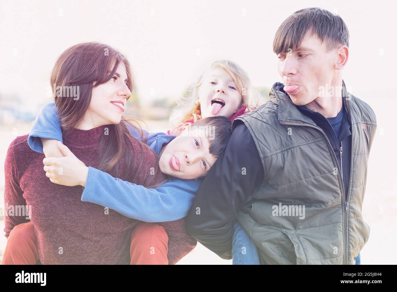 Parents and two kids having fun together - Family of fooling around and showing tongue - Dad mom and two kids hugging together happy family concept Stock Photo