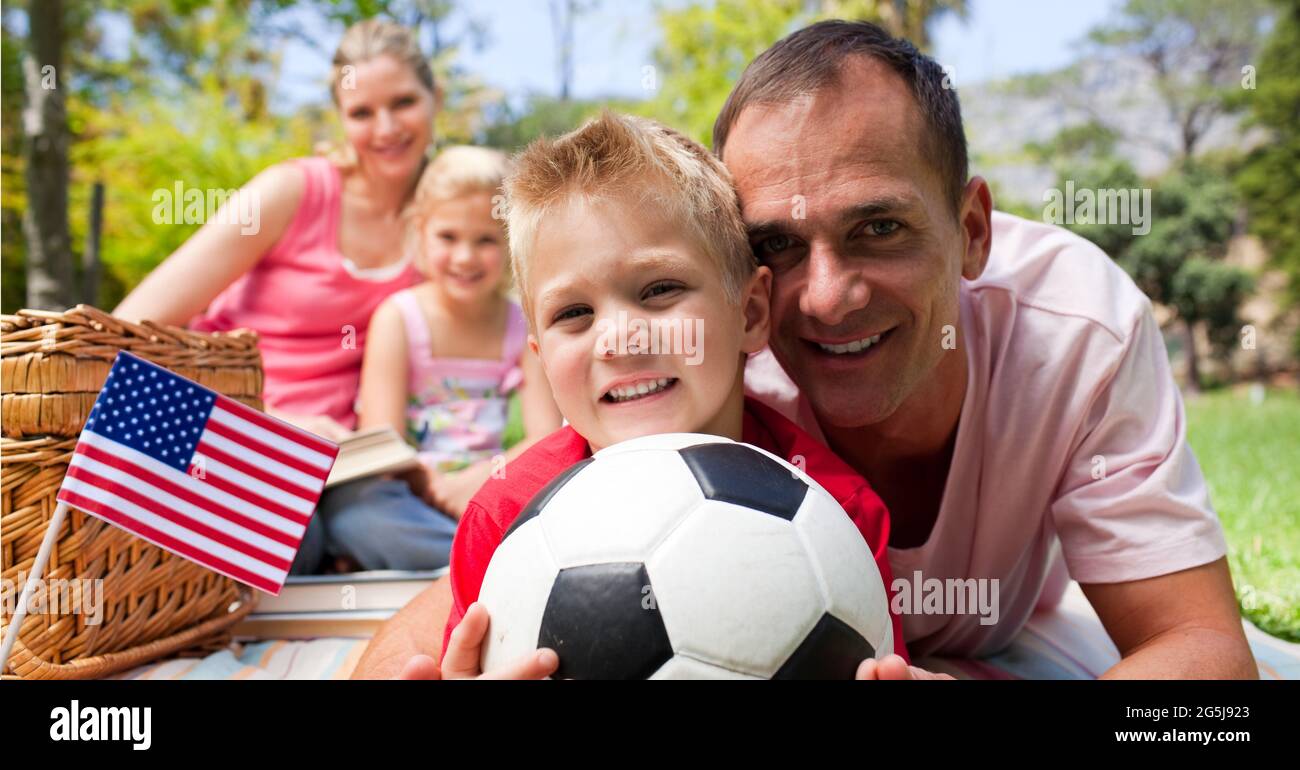 Composition of waving american flag, over happy family with football having picnic Stock Photo