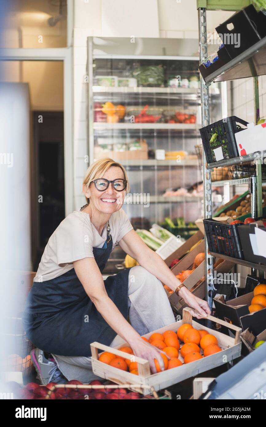 Portrait of smiling female owner arranging fruits in rack at store ...