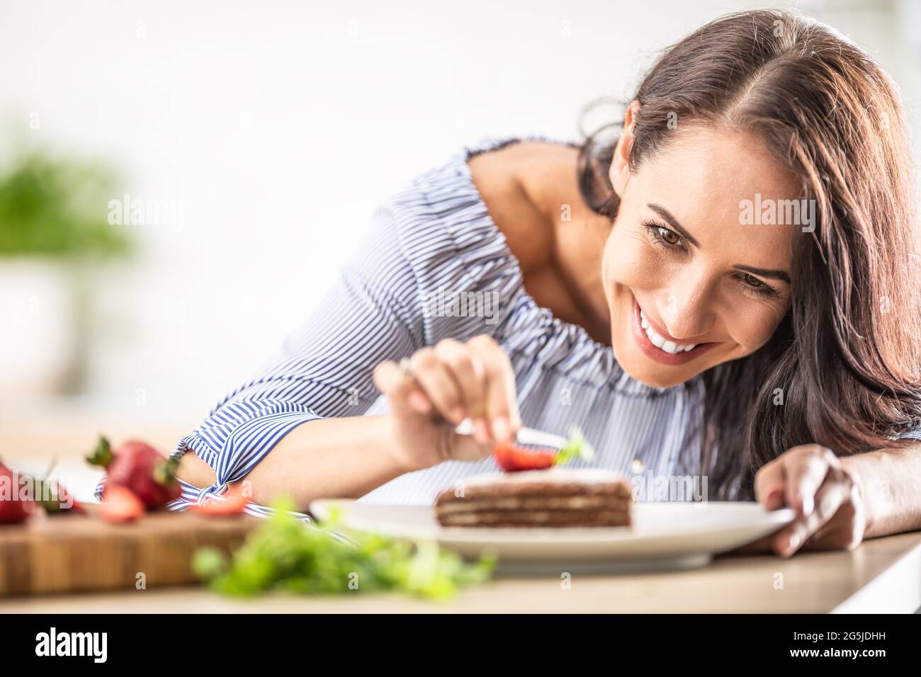 Smiling woman decorates finished cake with tweezers. Stock Photo