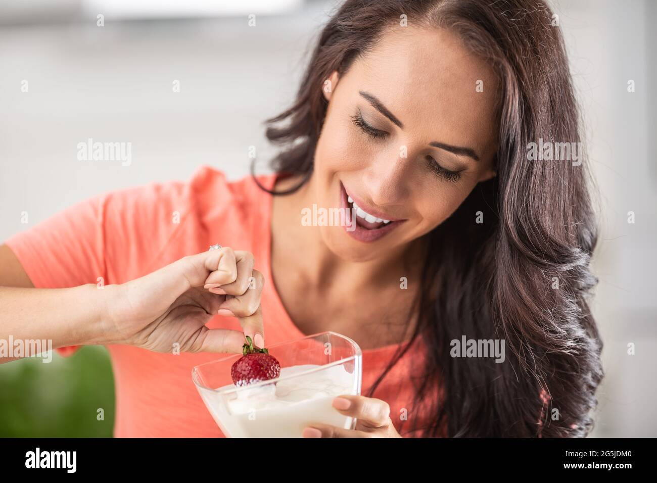 Young woman enjoys dipping fresh strawberry into a bowl of whipped cream. Stock Photo