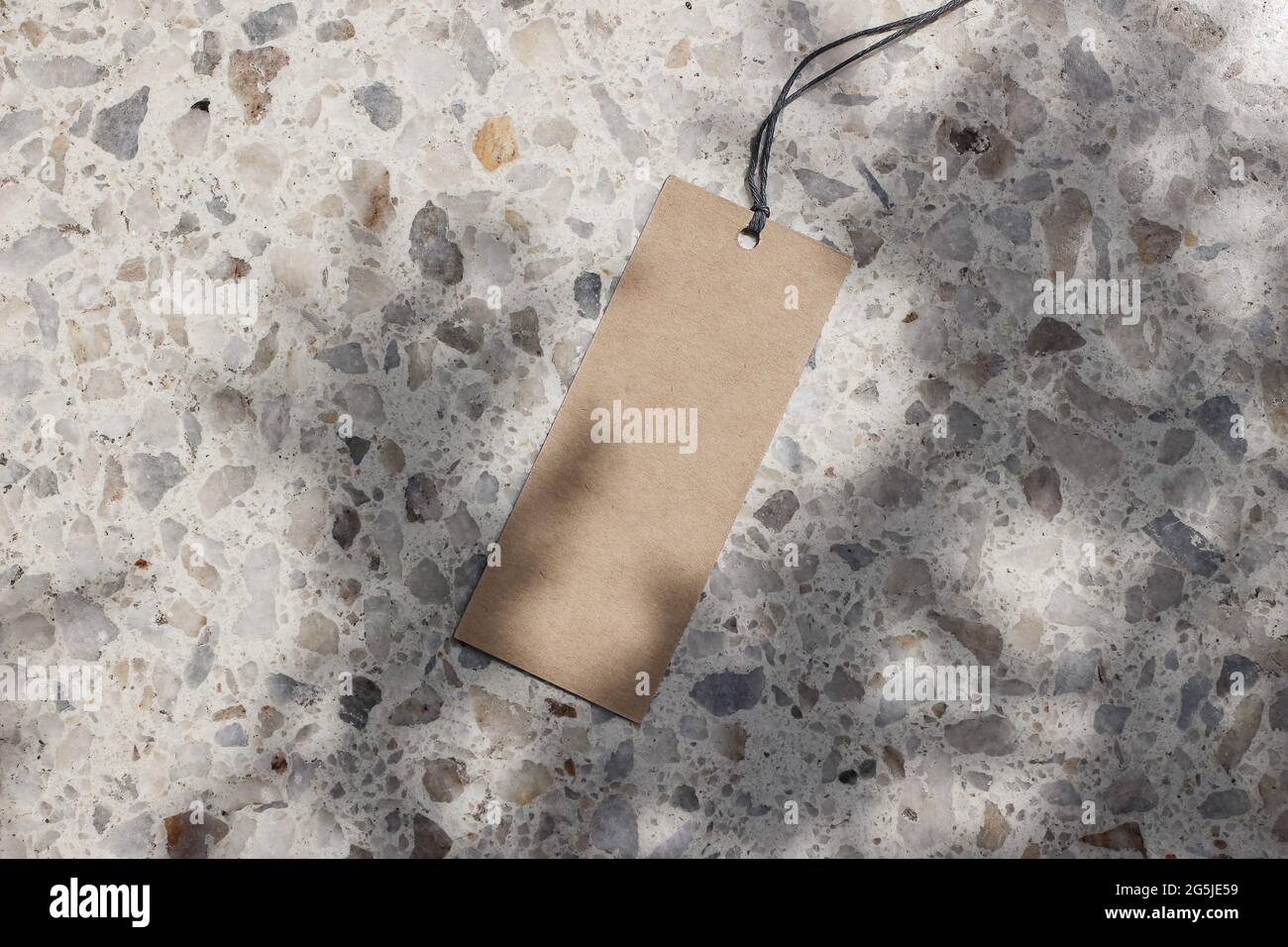 Blank craft paper gift tag, price label isolated in sunlight. Terrazzo background. Marble stone texture. Tree shadows overlay. Modern template Stock Photo
