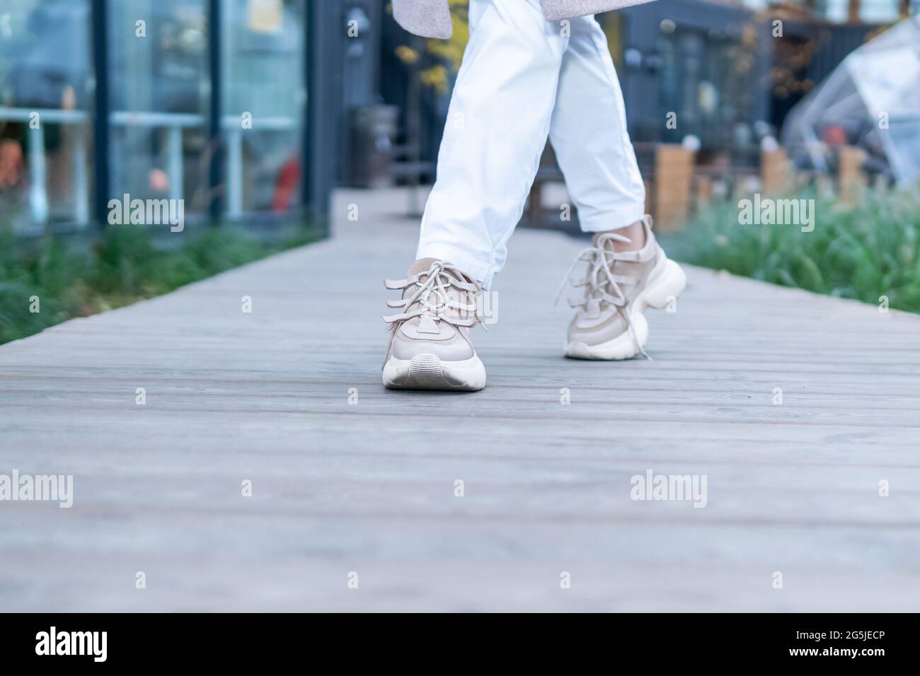 female legs in white sneakers walk along a wooden path towards the ...