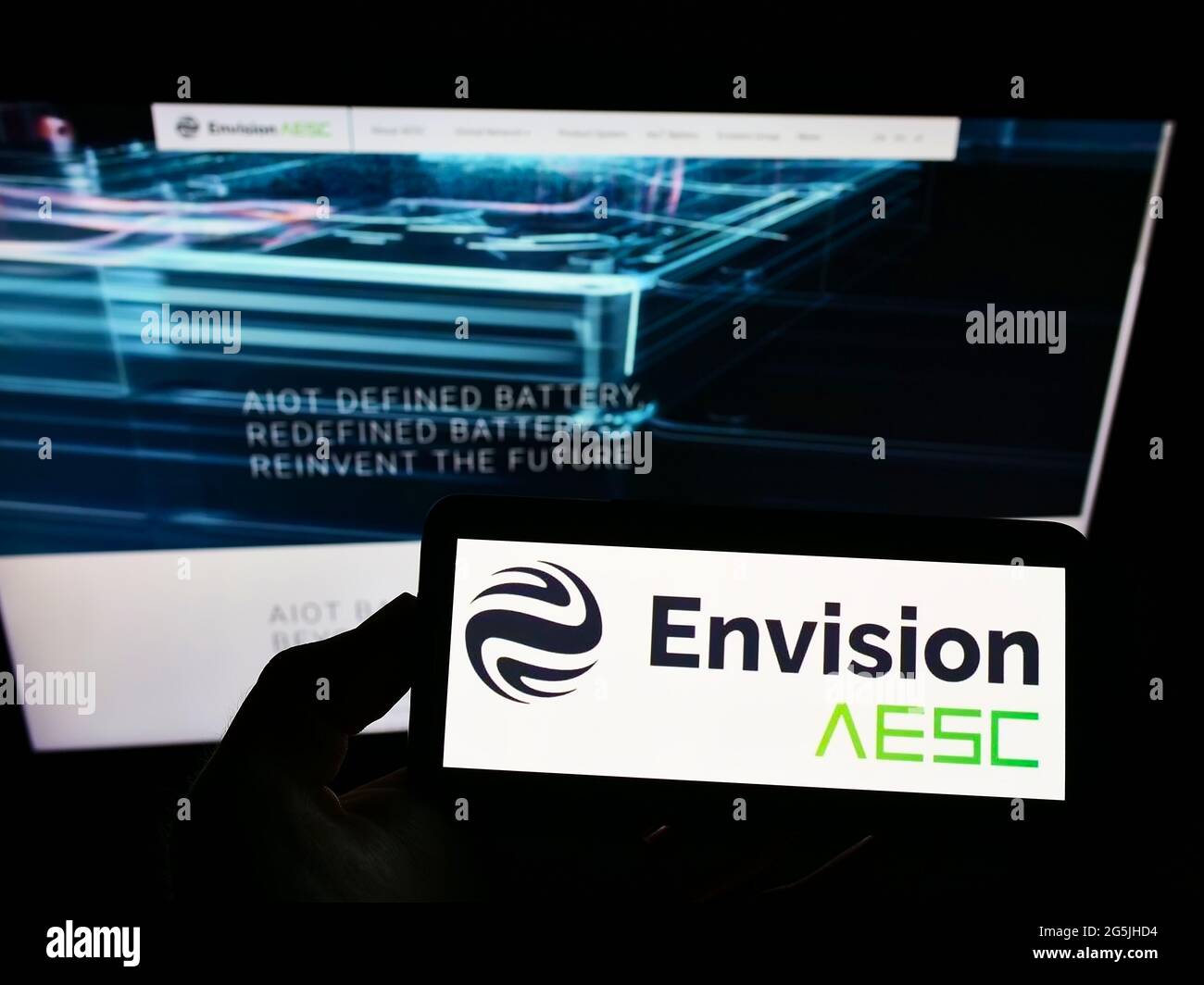 Person holding smartphone with logo of Automotive Energy Supply Corporation (Envision AESC) on screen in front of website. Focus on phone display. Stock Photo