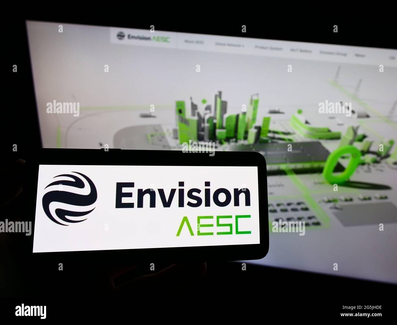 Person holding mobile phone with logo of Automotive Energy Supply Corporation (Envision AESC) on screen in front of webpage. Focus on phone display. Stock Photo