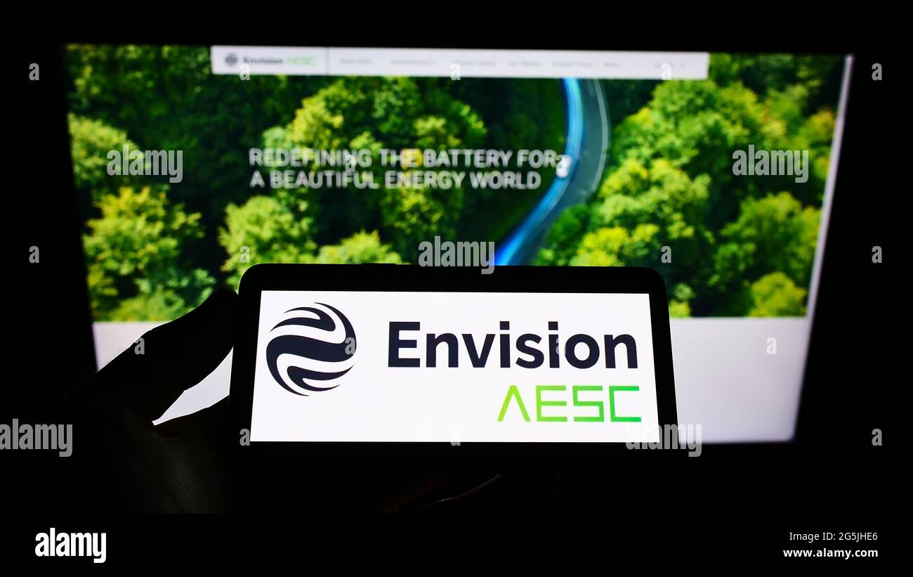 Person holding cellphone with logo of Automotive Energy Supply Corporation (Envision AESC) on screen in front of web page. Focus on phone display. Stock Photo