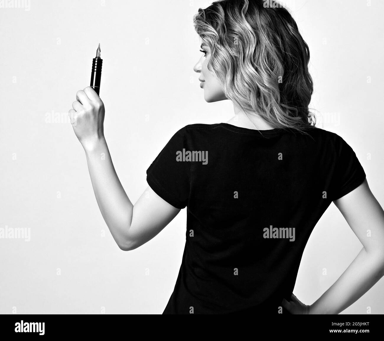 Black and white. Curly woman in black t-shirt stands with her back to camera holding permanent makeup machine Stock Photo