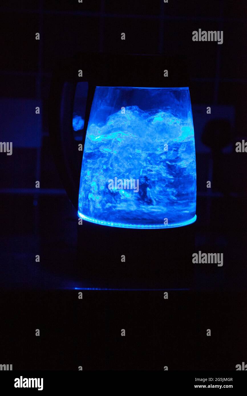 A see-through kettle boiling water, in the dark, illuminated only by a blue light inside Stock Photo
